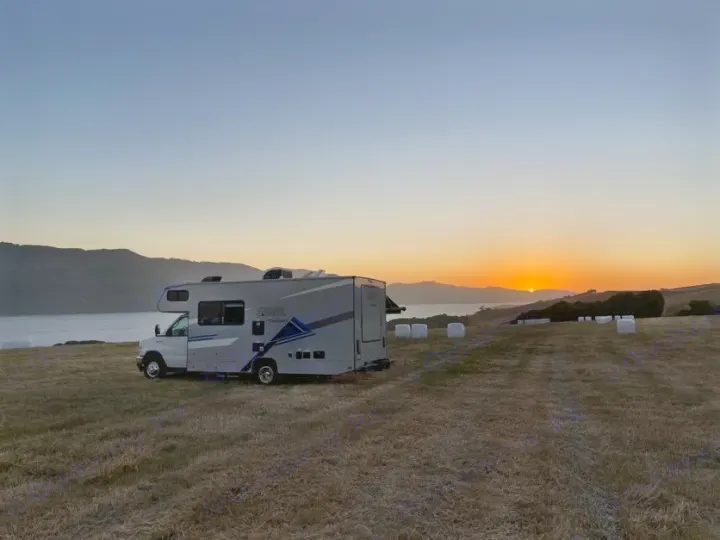 Serene RV rental view: Motorhome parked by a calm bay at sunset, surrounded by golden fields & hay bales.. Forest River Coachmen Crosstrail 2023