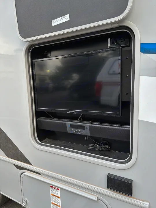 RV rental's outdoor entertainment: a mounted Furrion TV and soundbar in an exterior compartment for campsite viewing.. Forest River Coachmen Crosstrail 2023