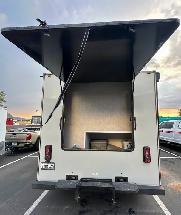 This RV rental's open rear hatch reveals spacious storage with bins, ideal for a versatile mobile unit.. Forest River Coachmen Crosstrail 2023