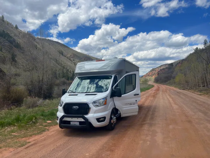 White RV rental on a scenic dirt road in mountains. Blue sky, fluffy clouds.. Coachmen Crosstrail 20XG 2022