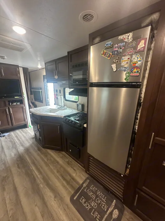 RV rental kitchen interior with stainless steel appliances, travel magnets on fridge, and an "Eat Well" mat.. Jayco Jay Flight SLX 2019