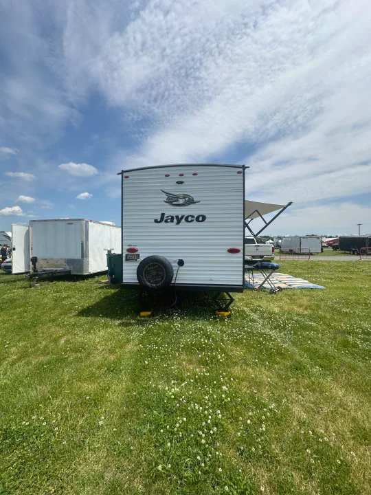 Jayco RV rental for outdoor adventures, parked on grass with a grill and other trailers nearby under a blue sky.. Jayco Jay Flight SLX 2019