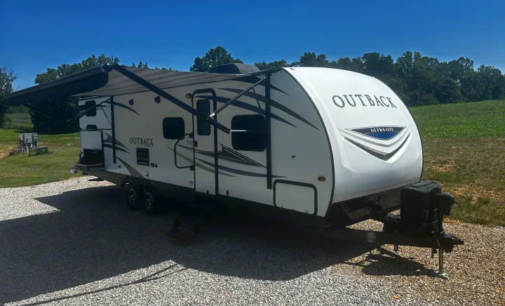 A pristine Outback Ultra-Lite RV rental travel trailer is ready for adventure, parked in a sunny, rural setting.. Keystone RV Outback Ultra-Lite 2018