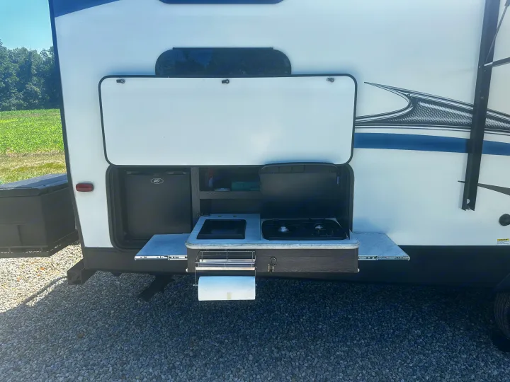 This outdoor kitchen of an RV rental features a fridge, sink, and two-burner stovetop, perfect for camping.. Keystone RV Outback Ultra-Lite 2018