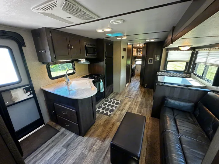 Tour this RV rental's cozy interior: a fully equipped kitchen, comfy leather sofa, and modern wood-style floor. Ready for adventures!. Keystone RV Outback Ultra-Lite 2018