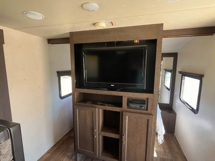 Cozy RV rental interior with an entertainment center (TV, stereo) and ample light from multiple windows.. Forest River Wildwood X-Lite 2018