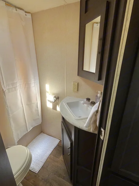 Compact RV rental bathroom with toilet, shower, sink, and vanity. Bright and functional space.. Forest River Wildwood X-Lite 2018