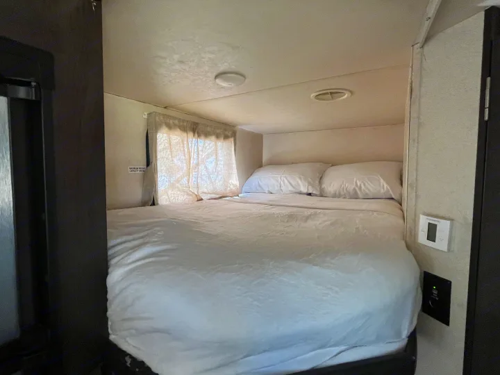 Compact RV rental bedroom with white bedding, window, climate control, and charging outlets. Max 350 lbs.. Forest River Wildwood X-Lite 2018
