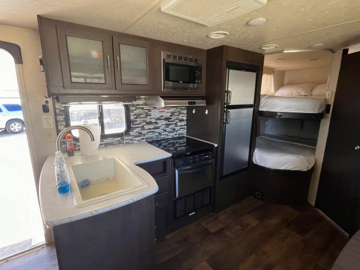 Spacious and modern RV rental interior with kitchen (sink, stove, microwave, fridge) and comfortable bunk beds.. Forest River Wildwood X-Lite 2018
