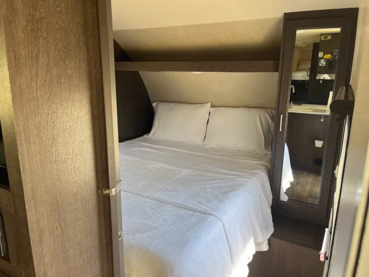 Cozy RV rental bedroom featuring a comfortable bed with white linens, overhead storage, and a mirrored wardrobe.. Forest River Wildwood X-Lite 2018