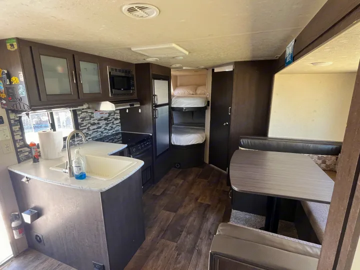 Spacious RV rental interior: kitchen with sink & microwave, cozy bunk beds, & dining area for comfortable travel.. Forest River Wildwood X-Lite 2018