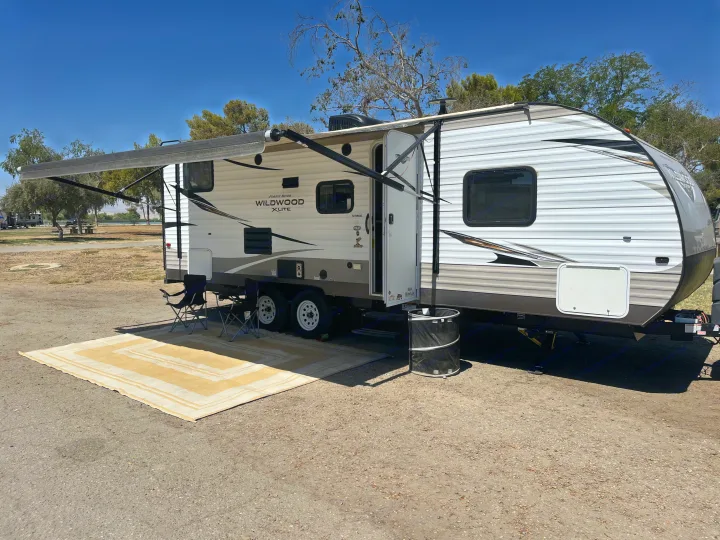 Spacious RV rental at a scenic campsite, with awning, chairs, and lake views. Perfect for your next outdoor adventure.. Forest River Wildwood X-Lite 2018
