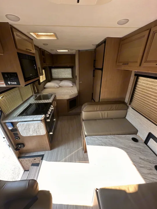 Spacious RV rental interior featuring a compact kitchen, comfortable bed, and versatile dinette, ideal for travel.. Thor Coleman 2021