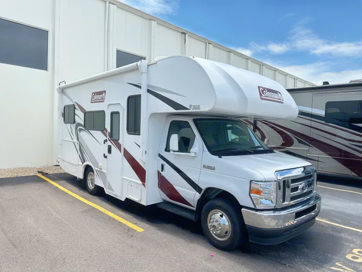 White Coleman Class C RV rental on Ford E-350 chassis, parked in a lot beside a building.. Thor Coleman 2021