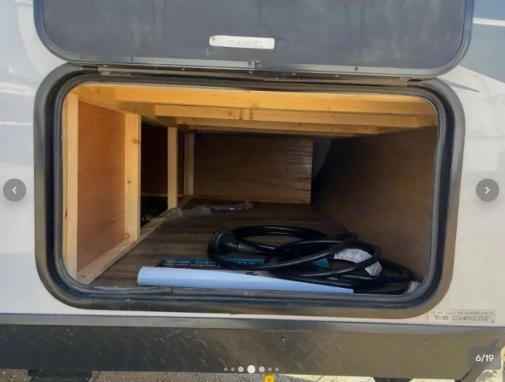 RV rental: View inside the spacious storage compartment, showing wood framing, an electrical cable, and manuals.. Forest River Cherokee Wolf Pup 16KHWBL 2024
