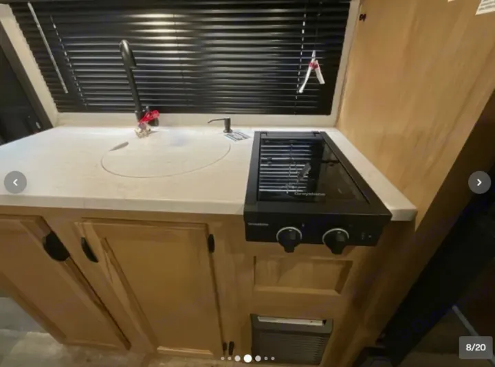 This RV rental kitchen features a light counter with a covered sink, a black faucet, and a two-burner stovetop. Light wood cabinets below.. Forest River Cherokee Wolf Pup 16KHWBL 2024