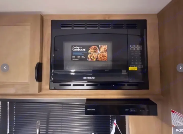 RV rental kitchen: Black Contoure microwave and Greystone range hood, built into light wood cabinets.. Forest River Cherokee Wolf Pup 16KHWBL 2024