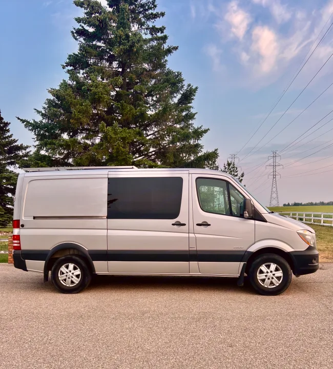 A silver Mercedes-Benz Sprinter camper van RV rental. Ideal for road trips, parked by trees and power lines.. Mercedes Sprinter 2016