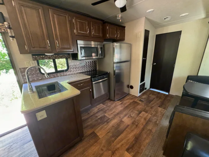 RV rental interior featuring a full kitchen with stainless steel appliances, wood-look floor, and inviting dining booth.. Forest River Salem Villa Classic Destination 2017