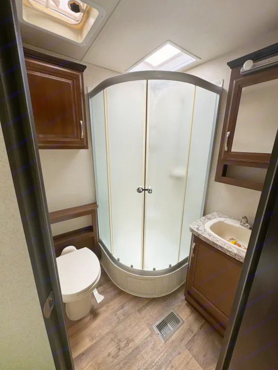 Compact RV rental bathroom features a corner shower with frosted doors, toilet, and vanity sink, all within a small, functional space.. Forest River Salem Villa Classic Destination 2017