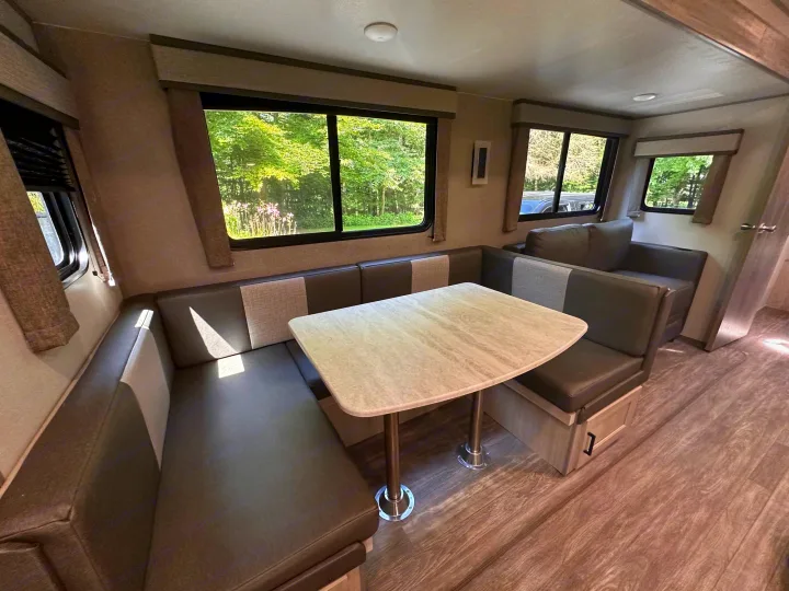 This RV rental interior features a spacious dinette with U-shaped seating and a table, perfect for meals with a view of nature.. Forest River Aurora 28BHS 2024