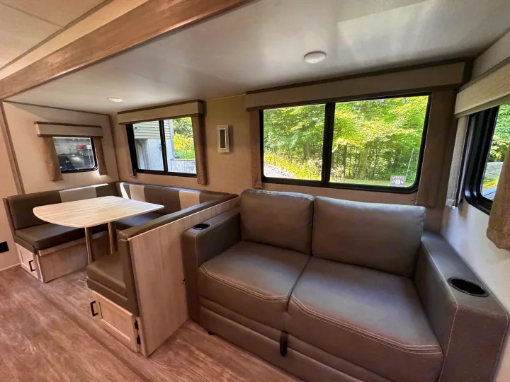 The interior of this RV rental features a comfortable dining booth with a table and a sofa with cupholders.. Forest River Aurora 28BHS 2024