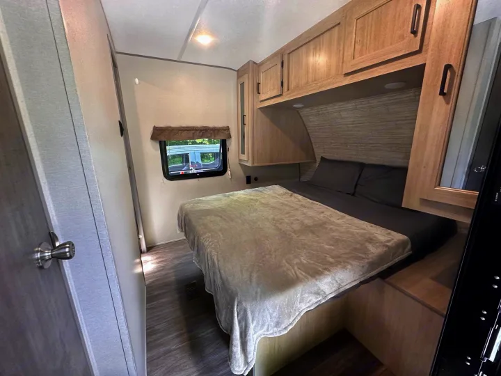 Cozy RV rental bedroom with a comfortable bed, overhead cabinets, and a window providing natural light. Perfect for travel.. Forest River Aurora 28BHS 2024