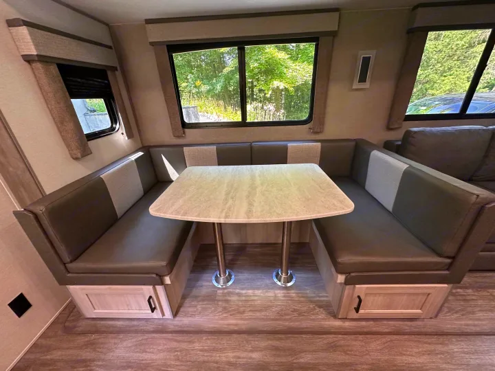Cozy RV rental dinette with U-shaped booth seating, a table, and large windows revealing an outdoor view.. Forest River Aurora 28BHS 2024
