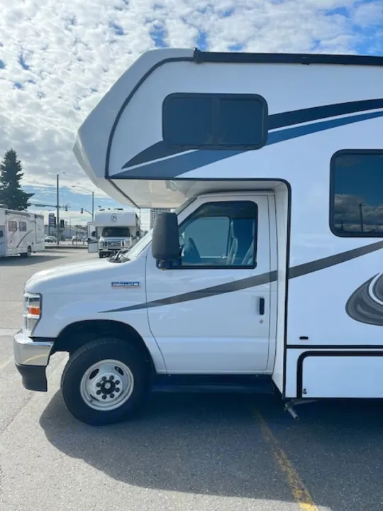 A clean white Class C RV rental, featuring blue and grey stripe accents, parked on asphalt under a cloudy sky.. Forest River Forester 2022