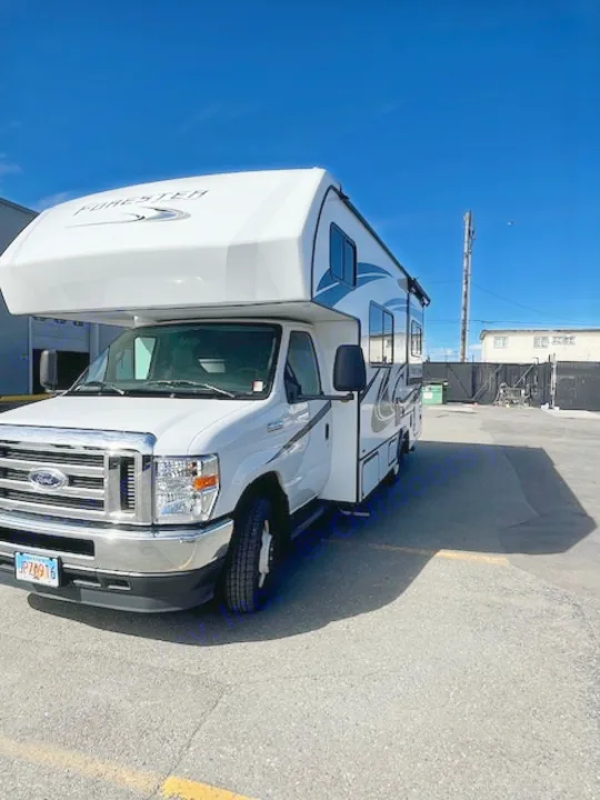 Bright white Ford Forester Class C RV for rental, parked outdoors on asphalt under a clear blue sky.. Forest River Forester 2022