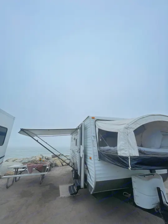 Beachside RV rental: A pop-out camper trailer by the foggy ocean, with awning & picnic table ready for a tranquil escape.. Forest River Wildwood 2011