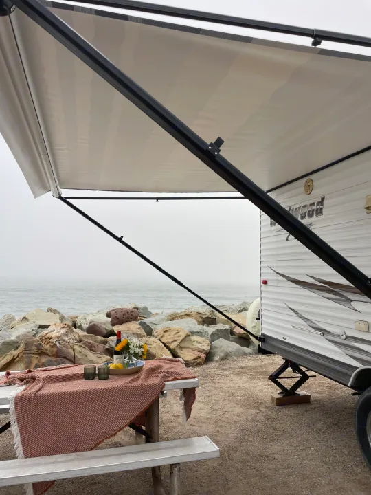 Scenic oceanside RV rental setup with an extended awning, a picnic table, and rocky beach views.. Forest River Wildwood 2011