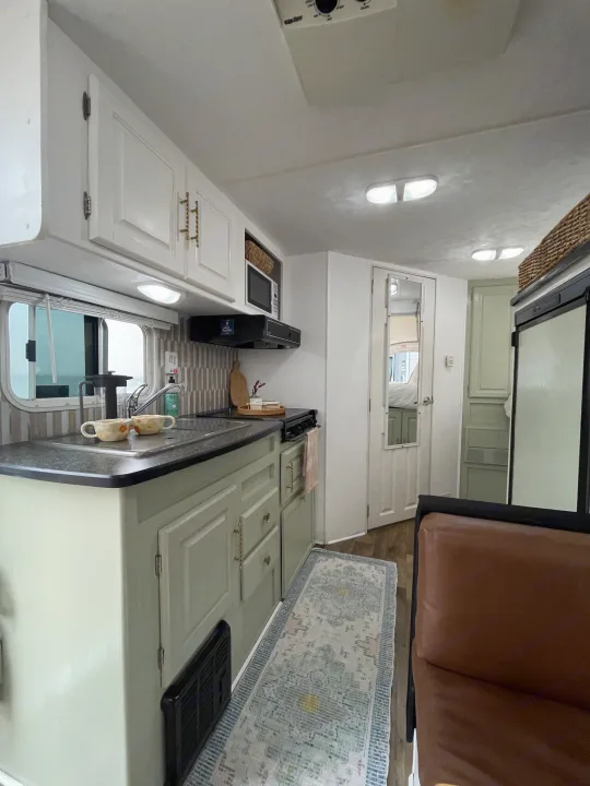 Stylish RV rental kitchen with sage green cabinets, modern tiled backsplash, and a cozy rug for mobile adventures.. Forest River Wildwood 2011