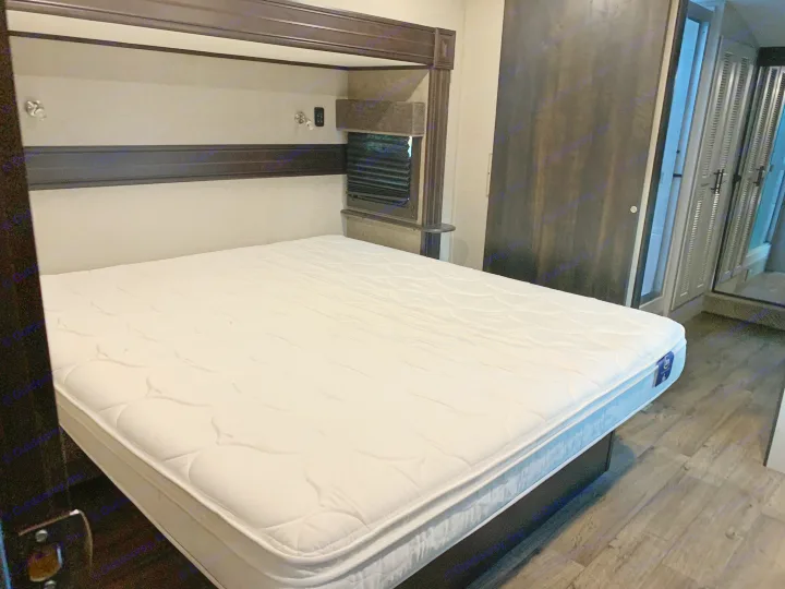 An inviting RV rental bedroom with a large white mattress on a dark bed frame, featuring dark wood accents and wood-look flooring.. Jayco Eagle 2020