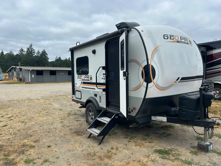 A light gray Geo Pro travel trailer rv rental is parked with its door open and steps down on a dirt lot.. Forest River Rockwood Geo Pro 2023
