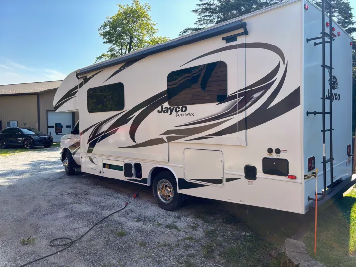 White Jayco Redhawk motorhome rv rental parked on gravel; ladder & power cord visible.. Jayco Redhawk SE 2022