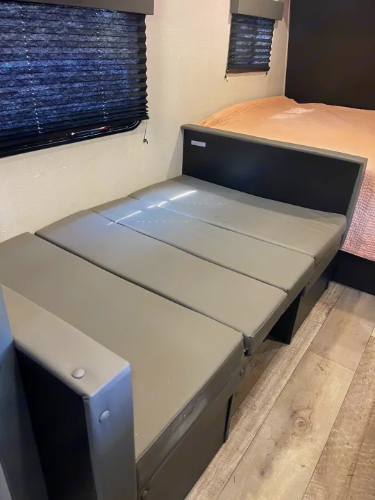RV rental: Versatile interior featuring gray convertible seating, a window with blinds, and a cozy bed.. Keystone RV Springdale 2022