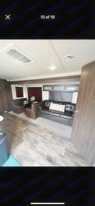 Spacious RV rental interior with a black sofa, dining booth, and wood laminate flooring. AC unit visible on ceiling.. Forest River Salem 2018