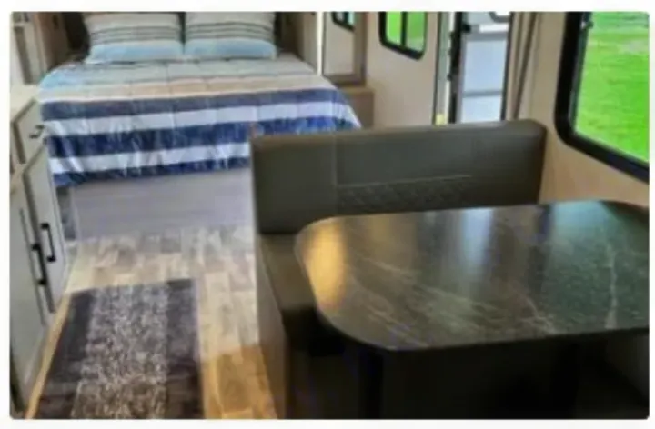 Cozy RV rental interior featuring a bed with striped bedding & a dark dinette area with bench seats & table.. Dutchmen Kodiak SE 2024