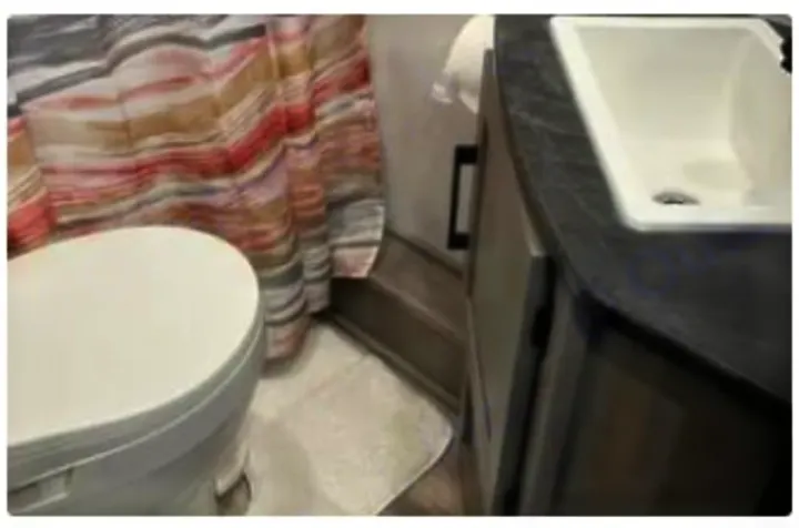 This RV rental bathroom features a toilet, shower with striped curtain, and a vanity with sink, offering comfort on your trip.. Dutchmen Kodiak SE 2024
