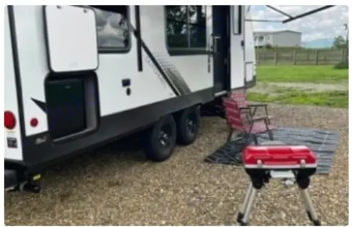 This RV rental is set up for camping. A white RV, red grill, chairs, and mat are ready for outdoor relaxation.. Dutchmen Kodiak SE 2024