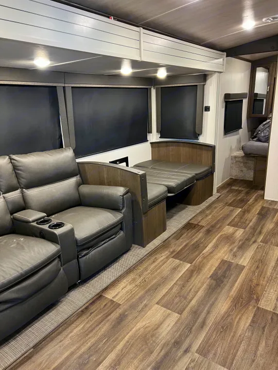 View of an rv rental's inviting interior: gray leather recliners, a dinette booth, and plank wood flooring.. Keystone RV Cougar 2023
