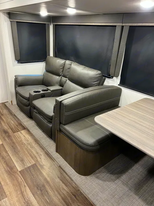 Modern RV rental interior: reclining theater seats with cup holders, dinette, wood floor, and dark shades.. Keystone RV Cougar 2023