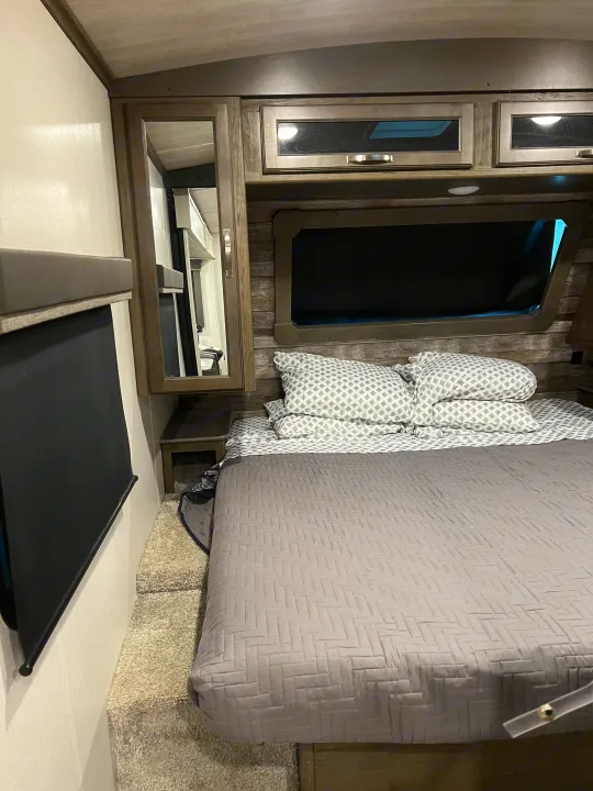 Explore this comfortable RV rental bedroom interior, featuring a cozy bed, window shades, and storage for your next trip.. Keystone RV Cougar 2023