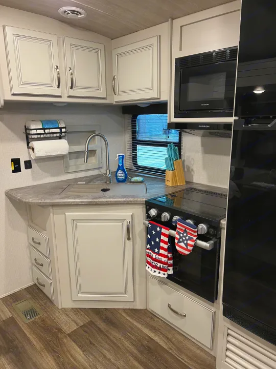 RV rental kitchen: light gray cabinets, sink, microwave, stove, fridge, and patriotic decor.. Keystone RV Cougar 2023