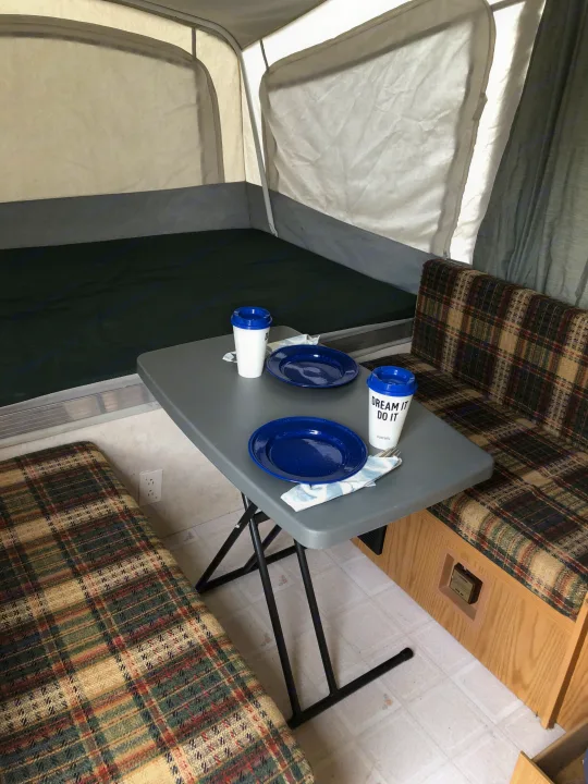 RV rental interior: a pop-up camper's compact dinette, bed, and table ready for use.. Coleman Destiny Taos 1999