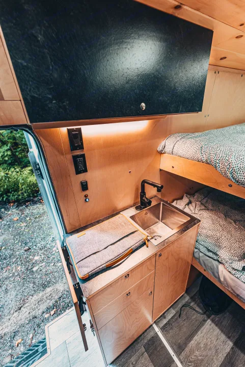 Inside a functional rv rental: compact kitchen with a sink, faucet, and bunk beds optimize space for travel.. Ford Van 2023