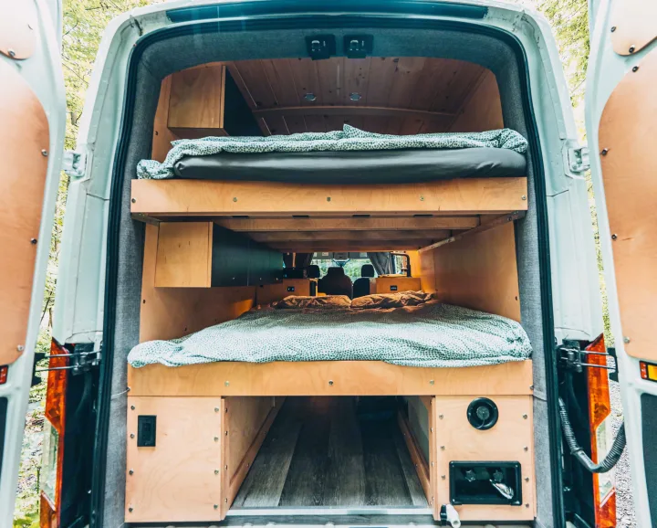 Inside this custom RV rental: cozy campervan bunk beds, wooden interior, viewed from the rear. Perfect for van life.. Ford Van 2023