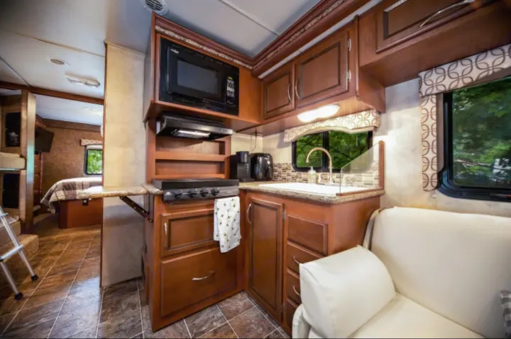 Spacious rv rental interior featuring a full kitchen with microwave, stove, and sink, plus a cozy living/bedroom area.. Other Four Winds 2013