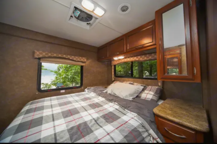 Comfortable RV rental bedroom with plaid bed, overhead storage, mirrored cabinet, and scenic window views. Ideal for travel.. Other Four Winds 2013